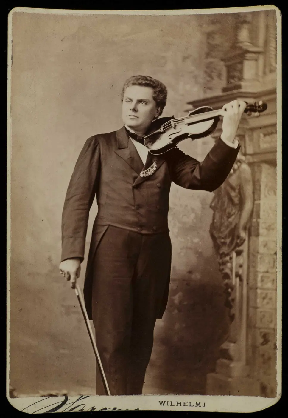 An old photograph of a man in a tailcoat standing with a violin raised to his shoulder and the bow lowered