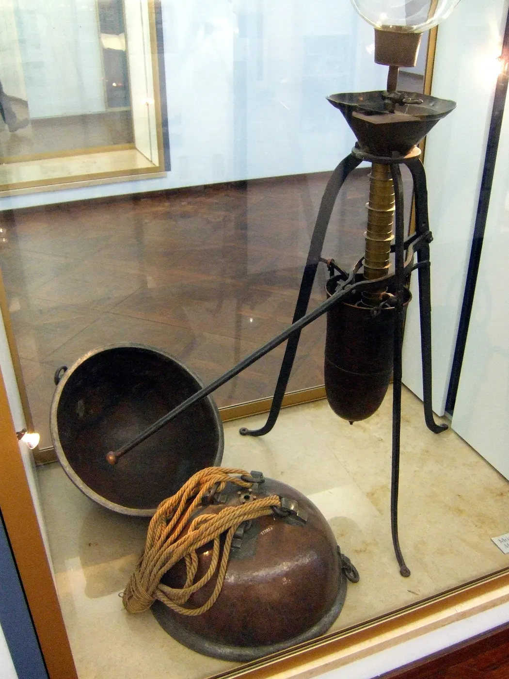Two copper hemispheres and a metal pump on a tripod on display in a glass case