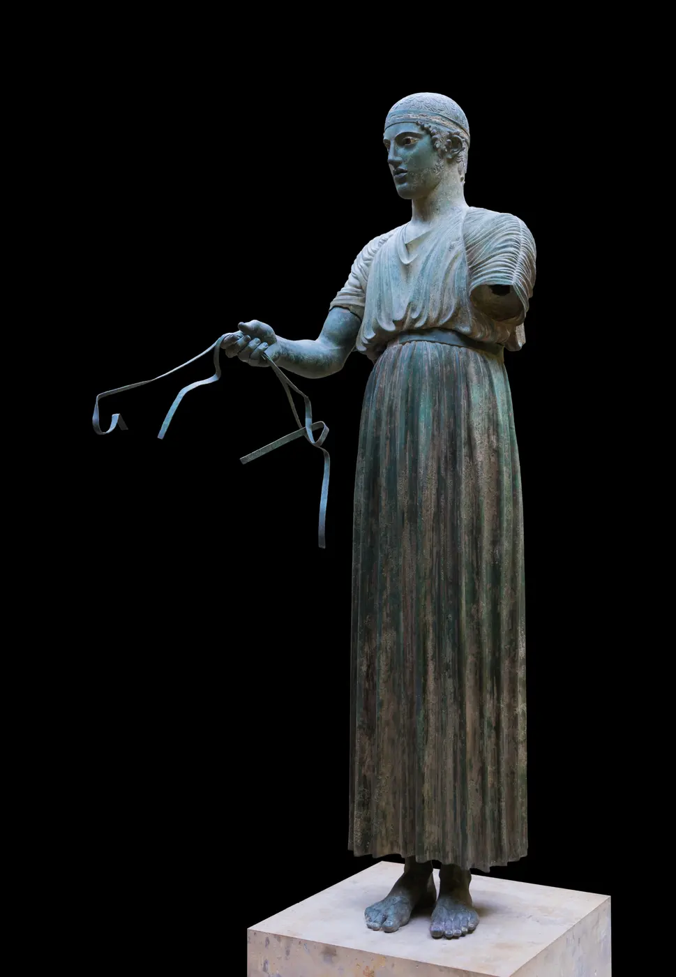 A bronze statue of a man standing in a long, finely pleated robe that reaches his ankles, holding reins in one hand
