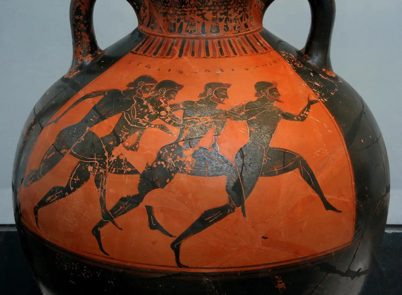 Four naked men painted in black on the red-brown body of a vase, running with their arms pumping