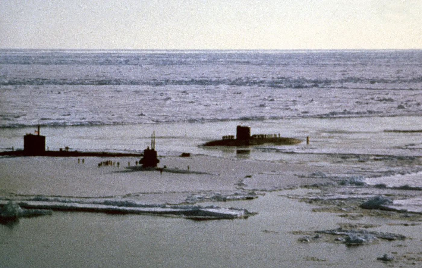 Several submarines that have broken up through the sea ice, with people walking nearby on the frozen surface