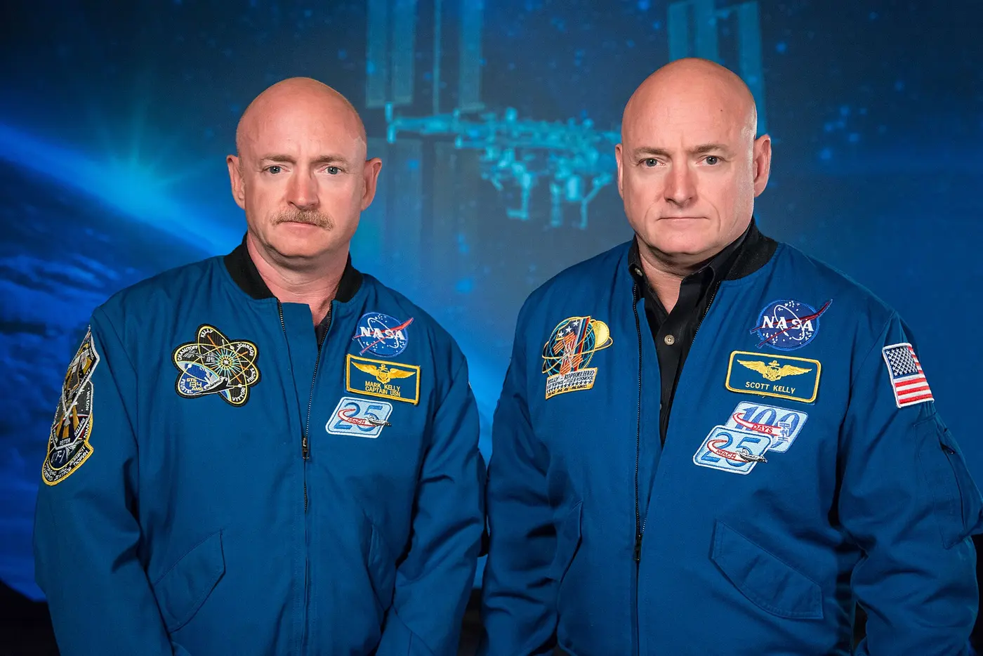 Two astronauts with strikingly similar faces standing side by side in blue jackets