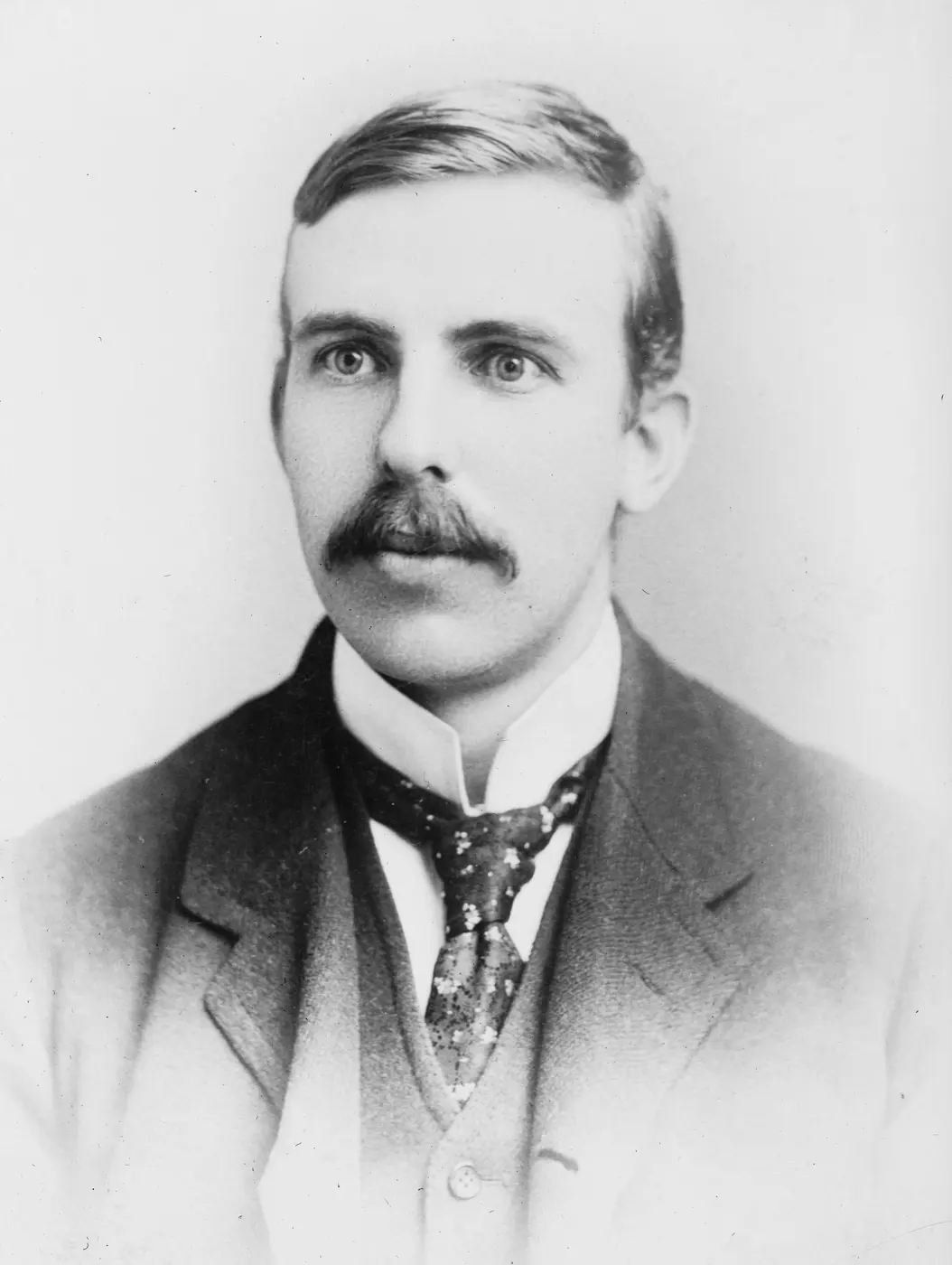Black-and-white portrait of a man with a mustache, wearing a suit and tie