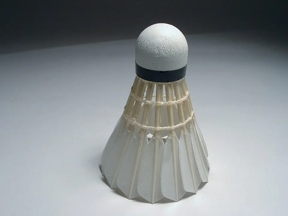 A shuttlecock standing on a white surface, cork on top, its white feathers spreading out in a cone