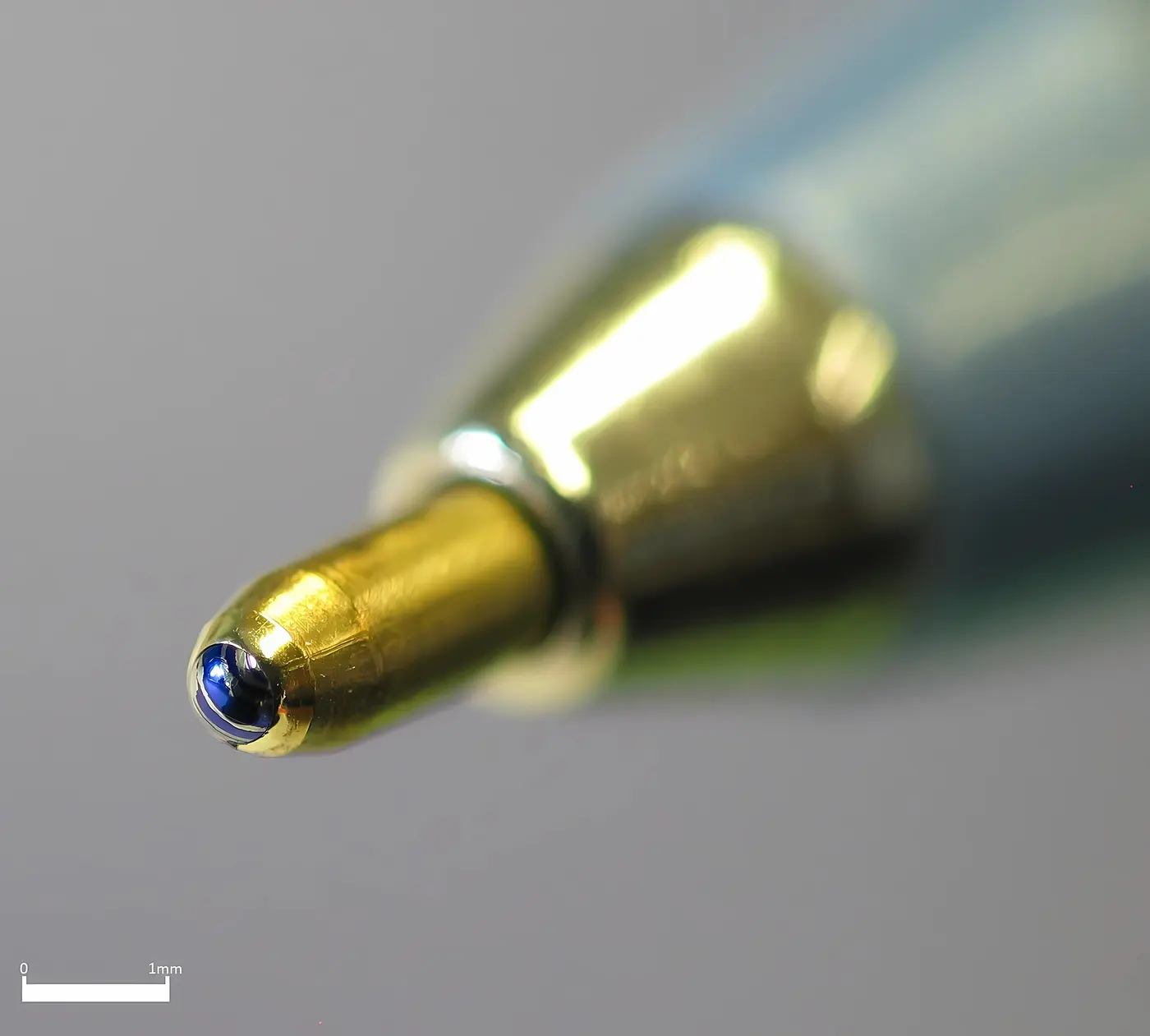A close-up of a gold-colored pen tip with a tiny blue ball set in its end