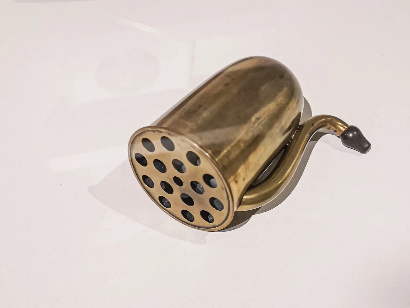 A small brass-colored hearing aid with a perforated cap and a curved tube