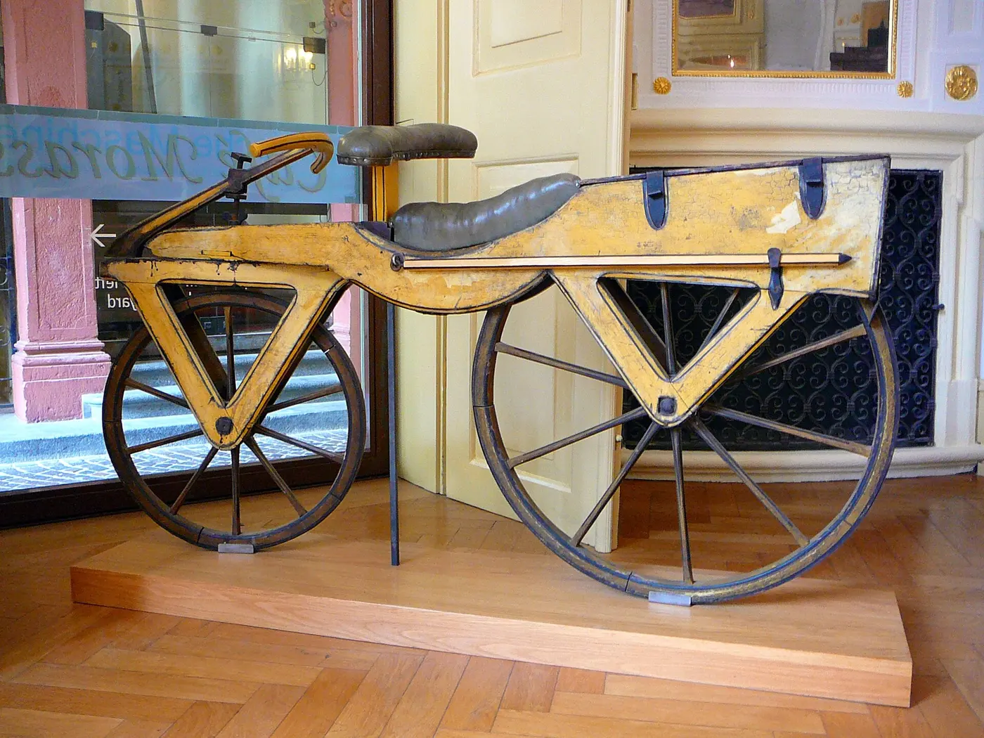 An old two-wheeled vehicle with a wooden frame, handlebar and saddle, but no pedals