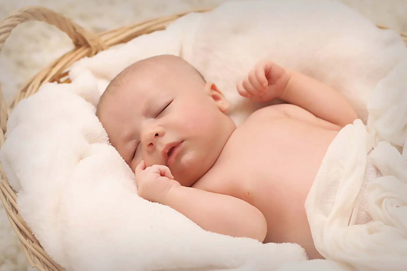A baby asleep with eyes closed in a basket lined with white cloth