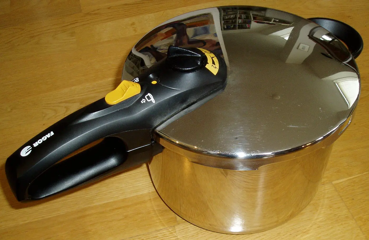 A stainless steel pressure cooker with a black handle and a pressure-control knob on the lid