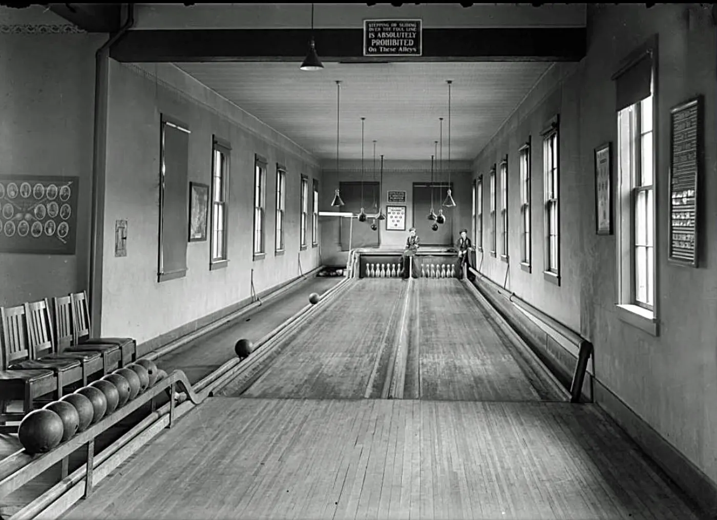 An old black-and-white photo of two long wooden lanes, with boys sitting beside the pins at the far end