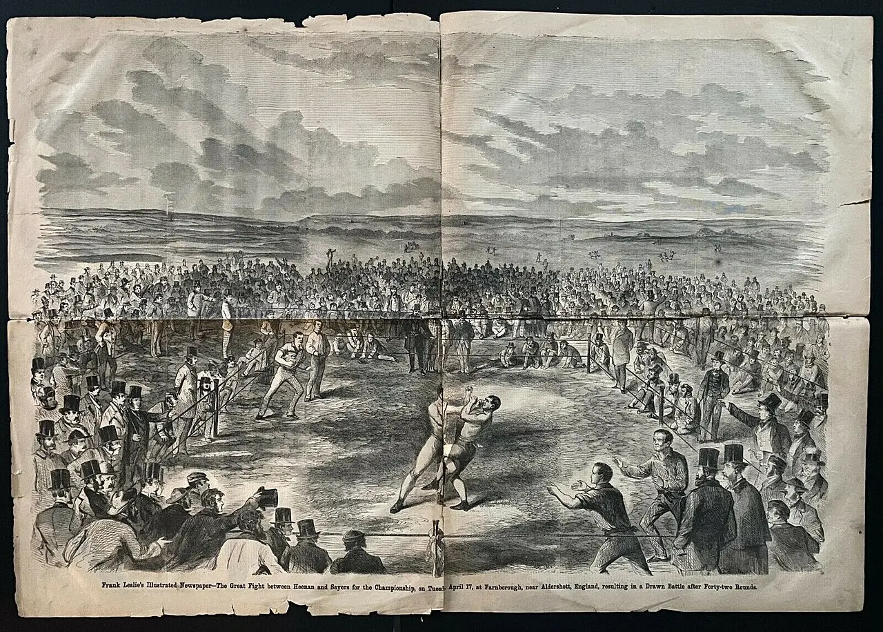 An engraving of two men grappling inside a square space marked out with stakes and ropes in an open field, surrounded by a huge crowd in hats