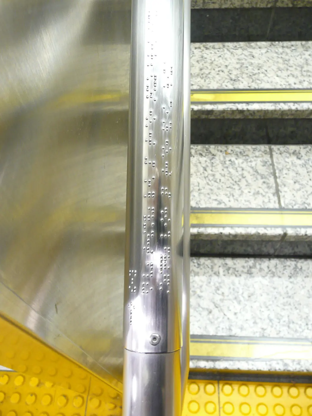Small braille characters lined up on a metal stair handrail