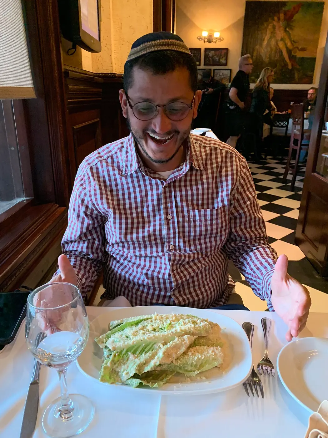 Whole romaine leaves coated with dressing and cheese laid out on a white plate, with a smiling man seated behind it