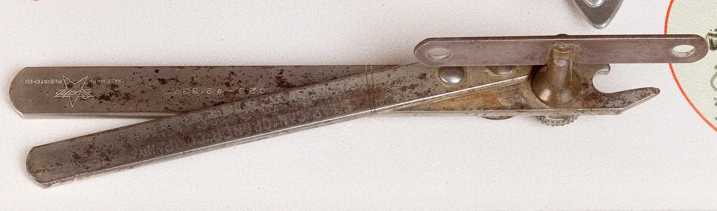 An old metal can opener with two long, slender handles and a small blade and gear at the end