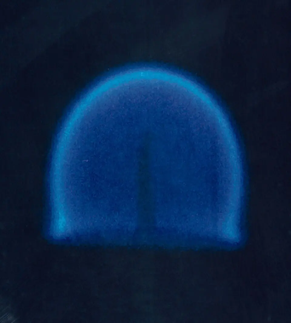 A faint blue flame shaped like a dome around a short wick against a dark background