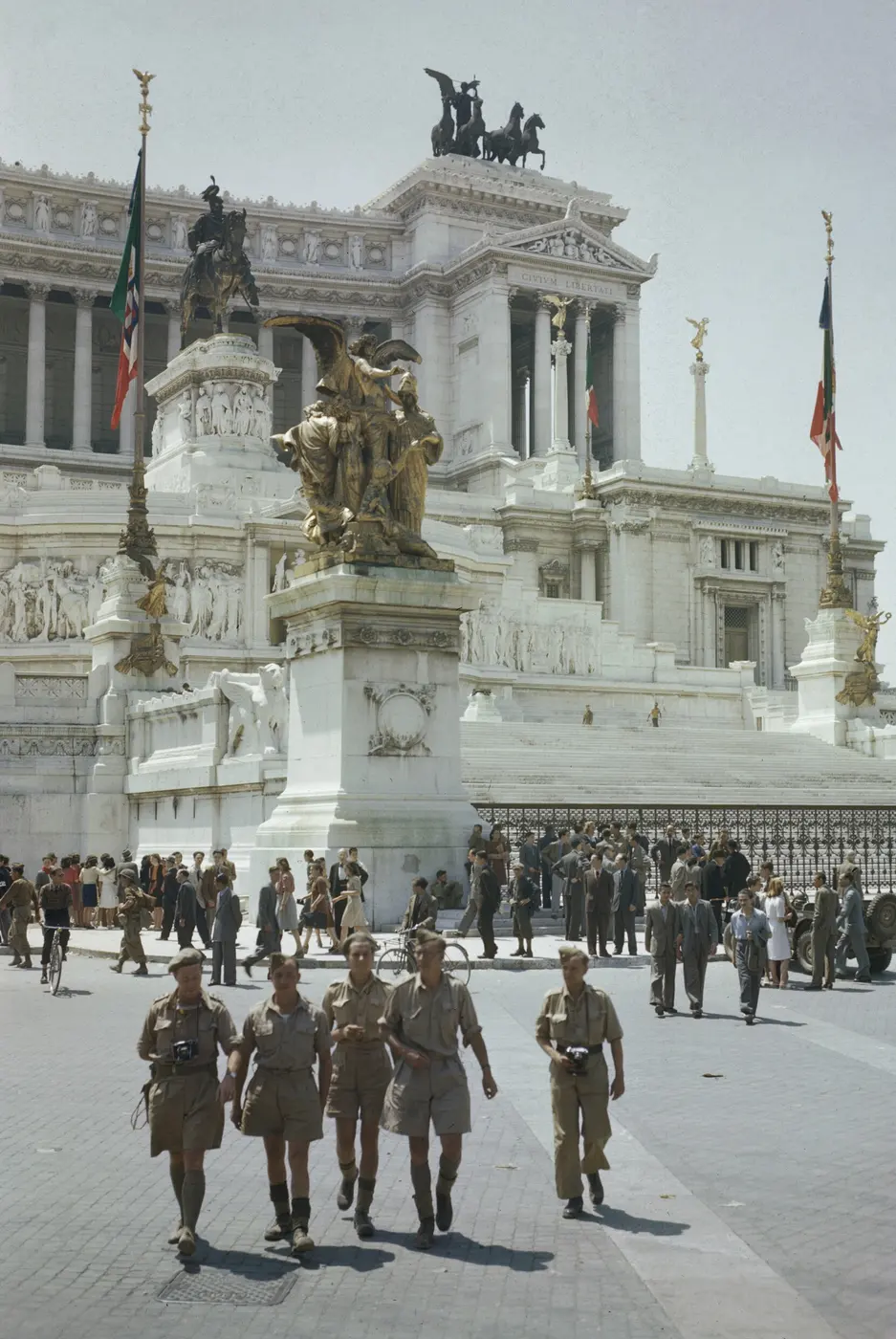 Soldiers in khaki uniforms walking in front of a huge white marble monument