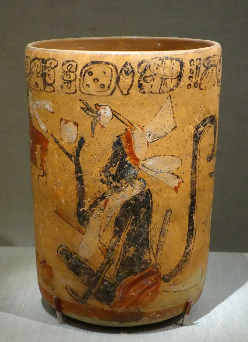 A cylindrical clay vessel painted with monkeys and a cacao tree, with a band of glyphs around the rim