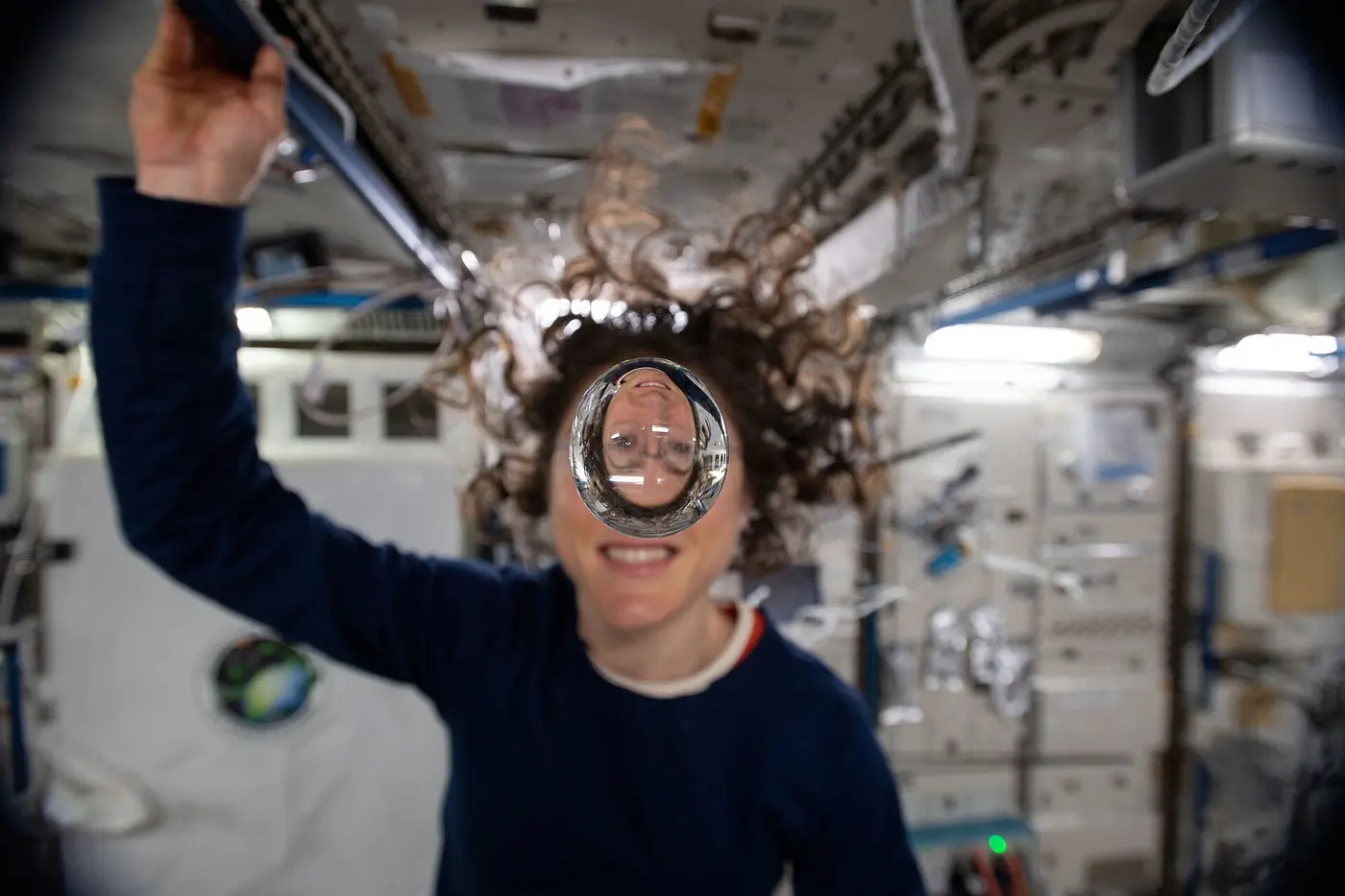An astronaut in a space station laboratory looking at a round ball of water floating in front of her face