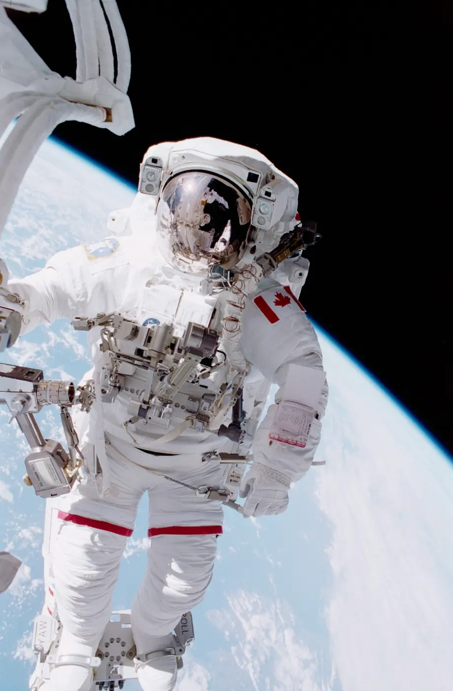 An astronaut in a spacesuit with a Canadian flag on the shoulder, working outside with Earth in the background