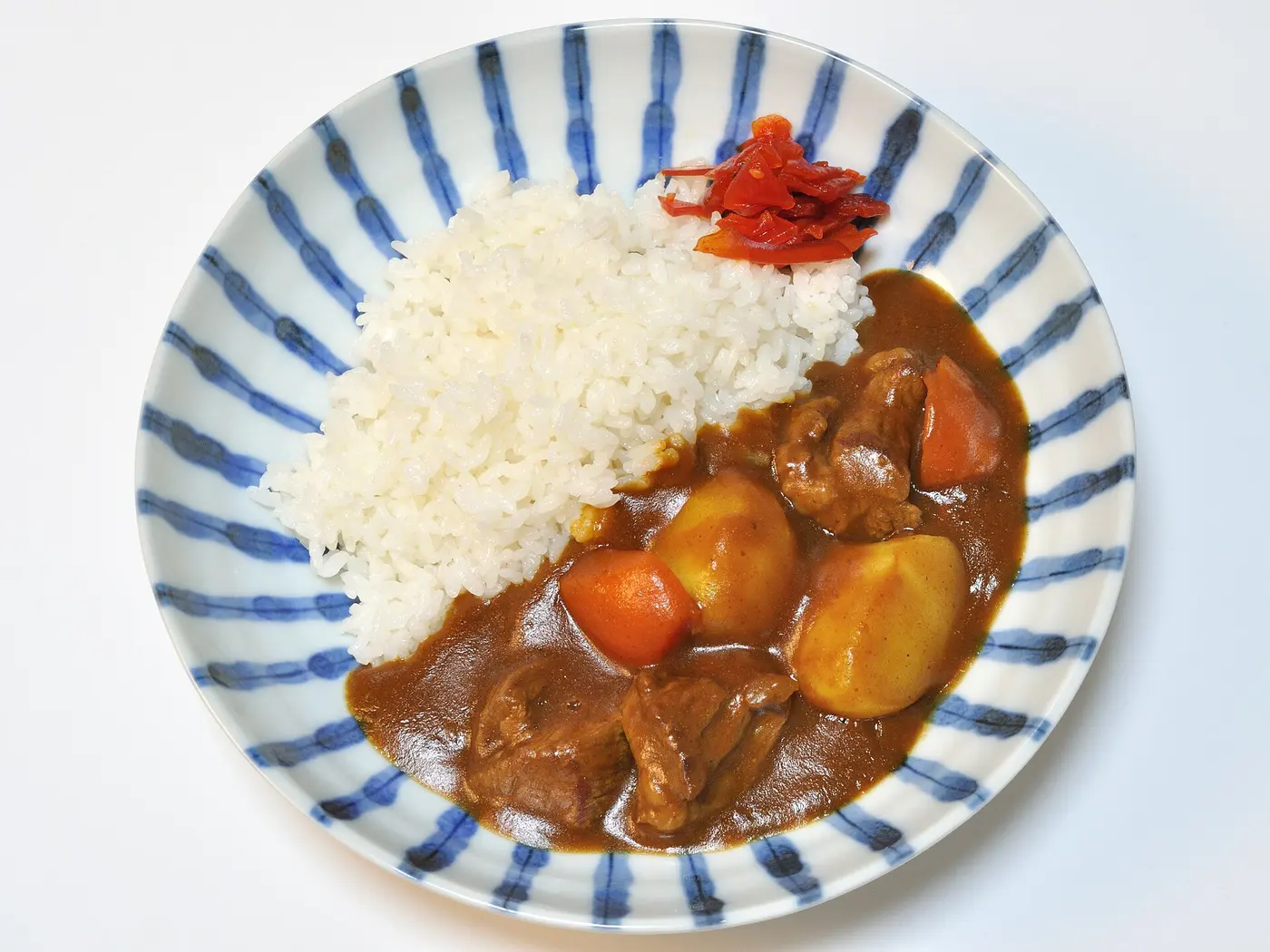 A plate of white rice with a thick curry containing beef, potatoes and carrots poured beside it