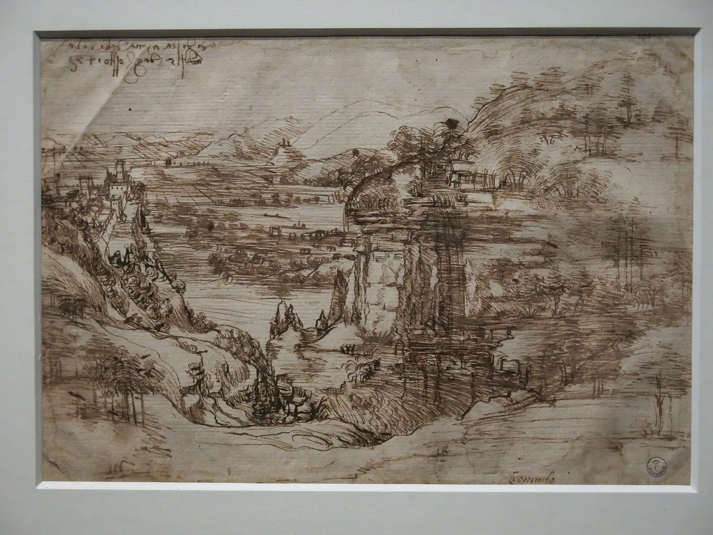 A brown-ink landscape drawing of a river valley with rocky hills and a distant plain, with two short lines of writing in the upper left
