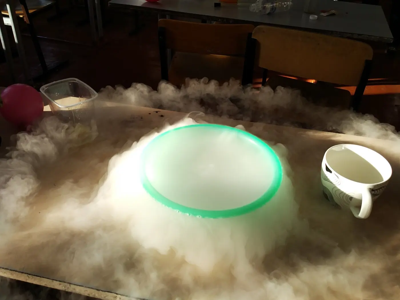 White fog overflows from a bowl on a table and spreads low across the whole tabletop