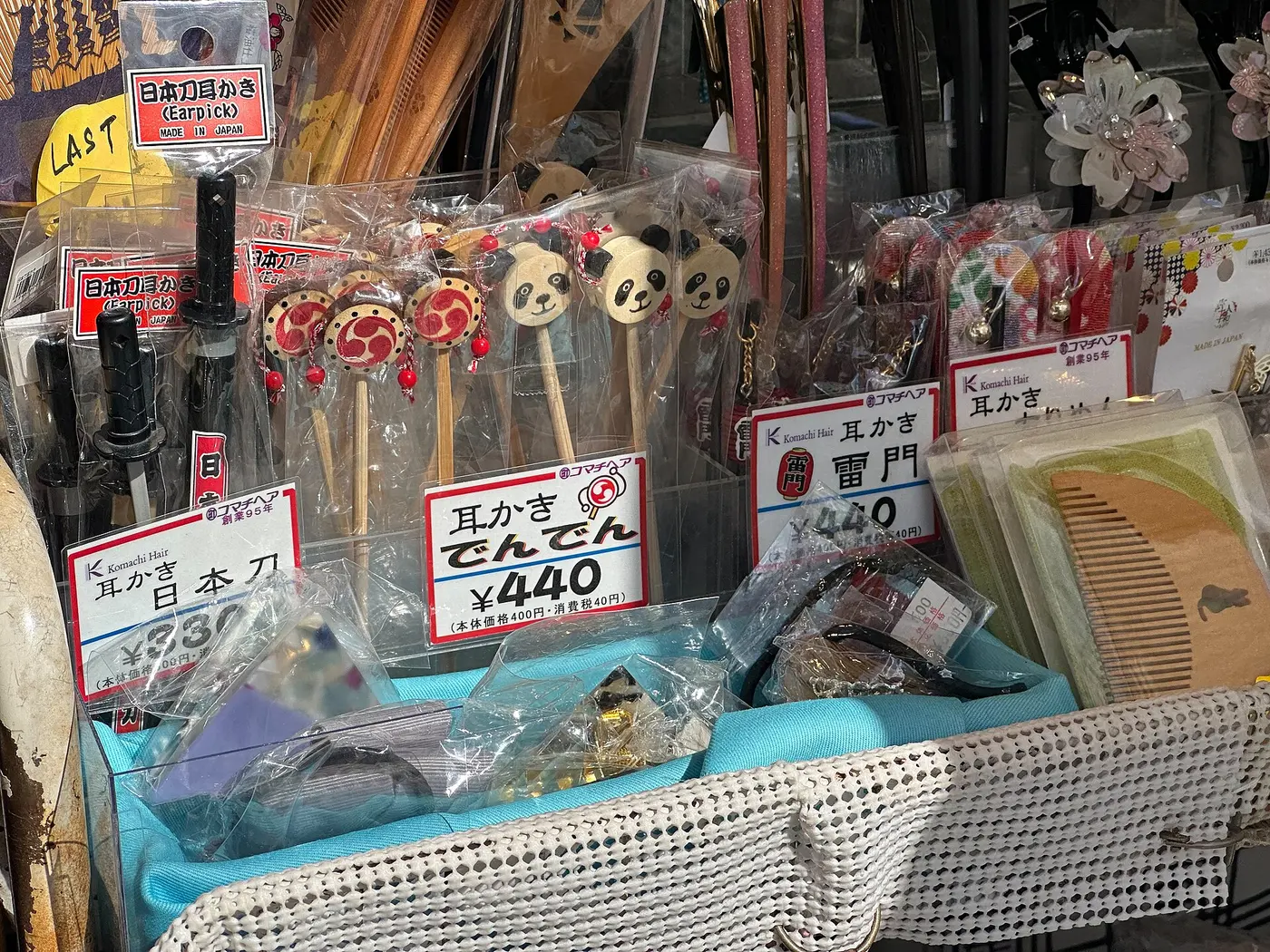 Wooden ear picks topped with pandas and drums, and ear picks shaped like Japanese swords, displayed with price tags in a basket at a shop