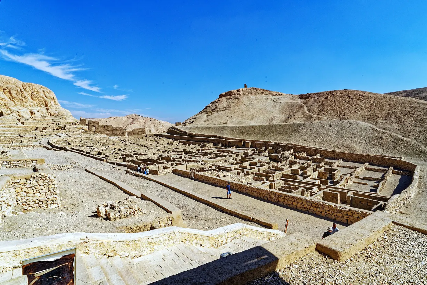 Ruins of stone house foundations laid out in blocks at the foot of dry rocky hills