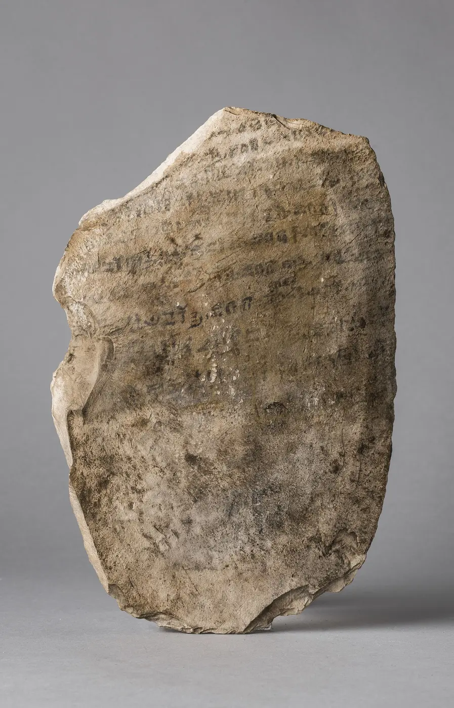 A pale brown limestone flake with several lines of faded black writing