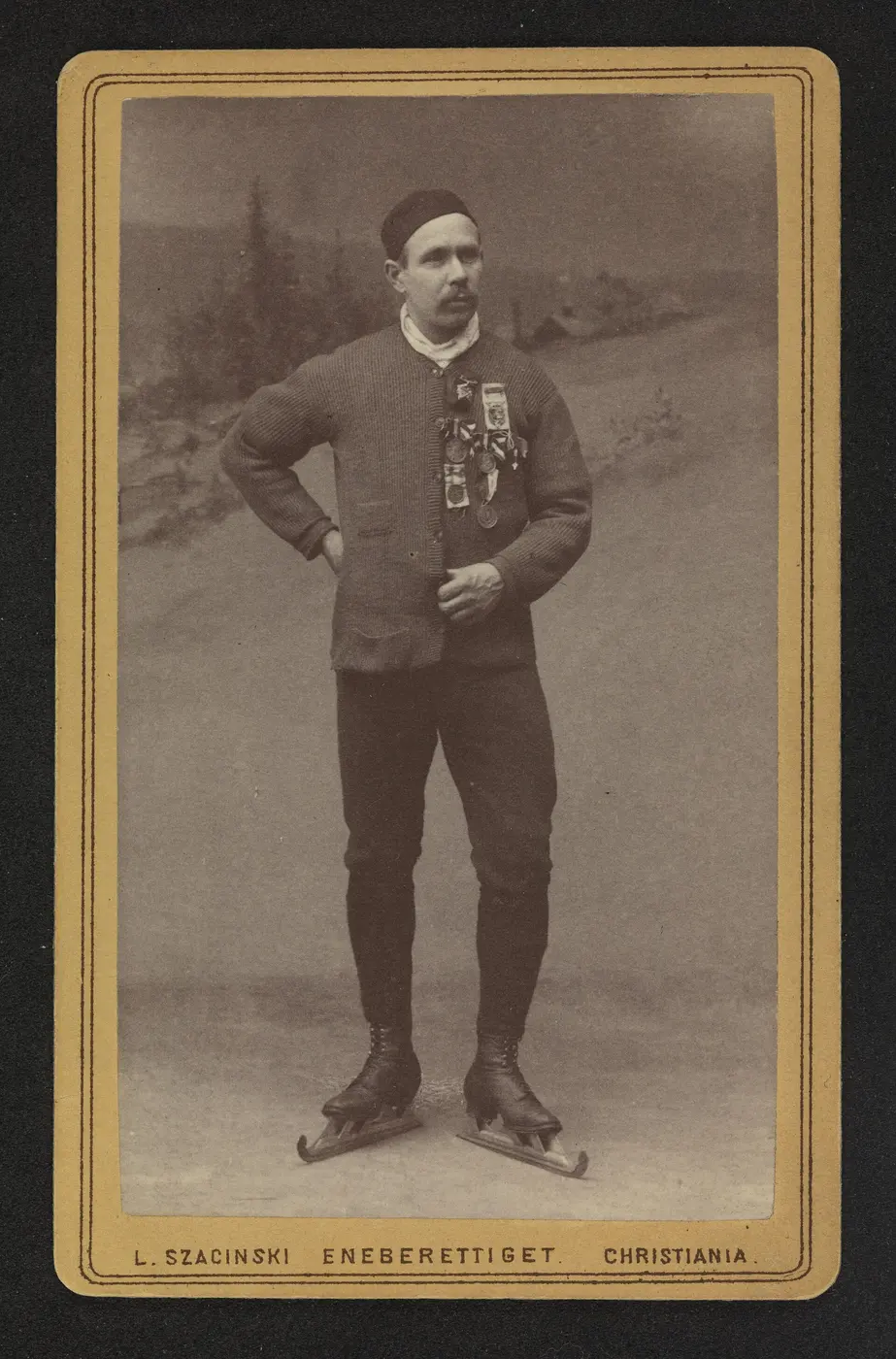 An old portrait photo of a mustached man in a sweater, wearing skates with long blades