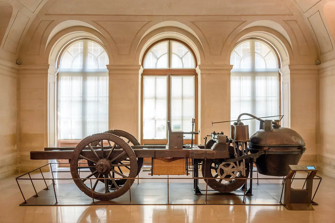 A large three-wheeled wooden vehicle carrying a big copper boiler at the front