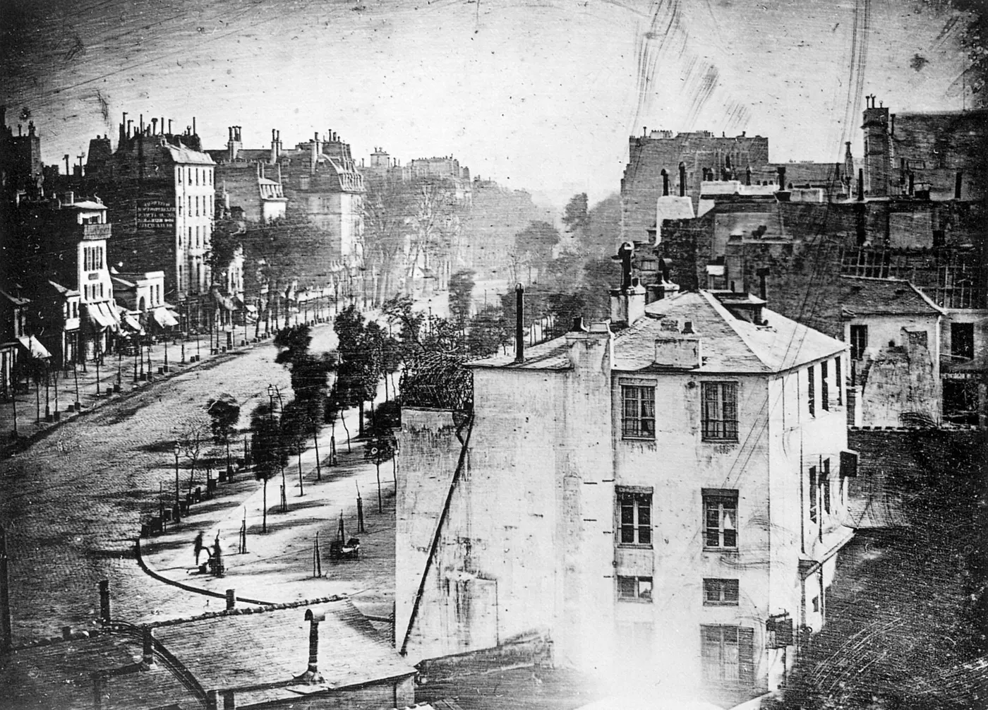 An old photograph, taken from high up, of an empty boulevard lined with trees and buildings