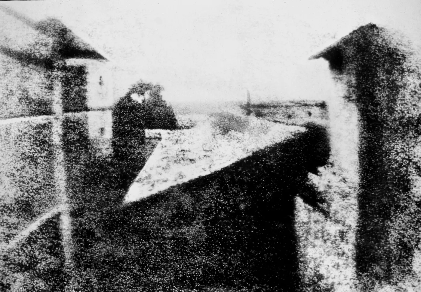 A grainy black-and-white scene with the hazy walls and roofs of buildings on the left and right