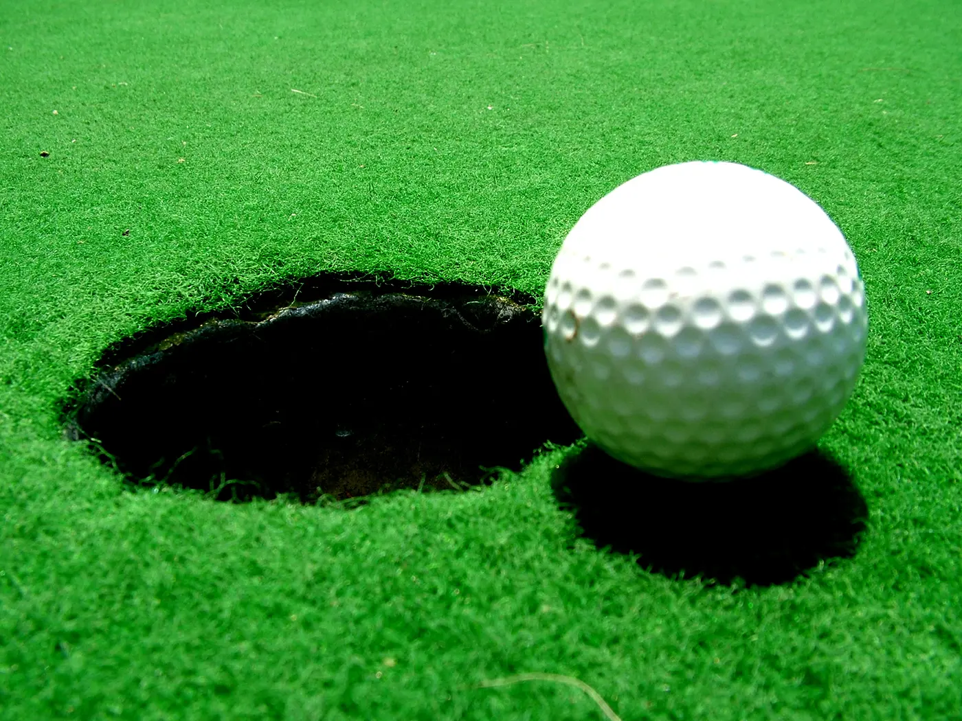 A white dimpled golf ball resting on the grass right beside the hole