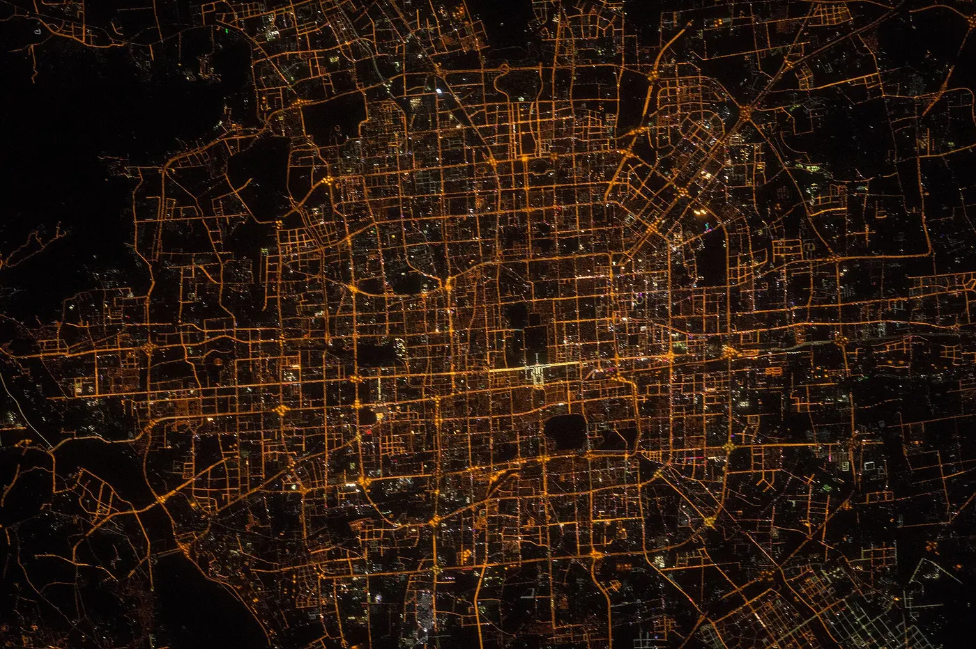 A city at night, its orange streetlights spreading out in a grid-like mesh against the darkness