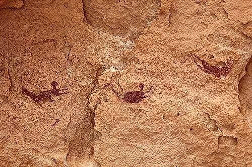 Several small dark-brown human figures painted on reddish rock, their limbs outstretched as if swimming