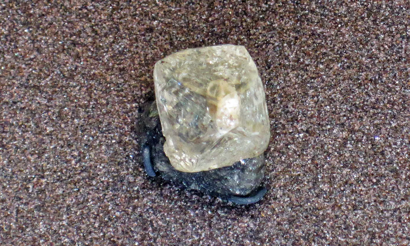 A yellowish, translucent diamond crystal resting on a sandy background