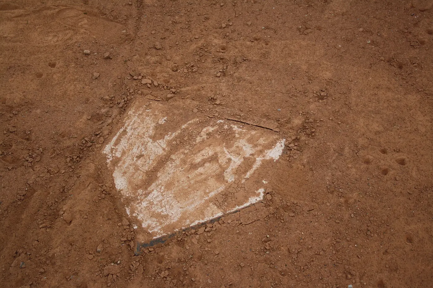 A white pentagonal home plate set into red clay and partly covered with dirt