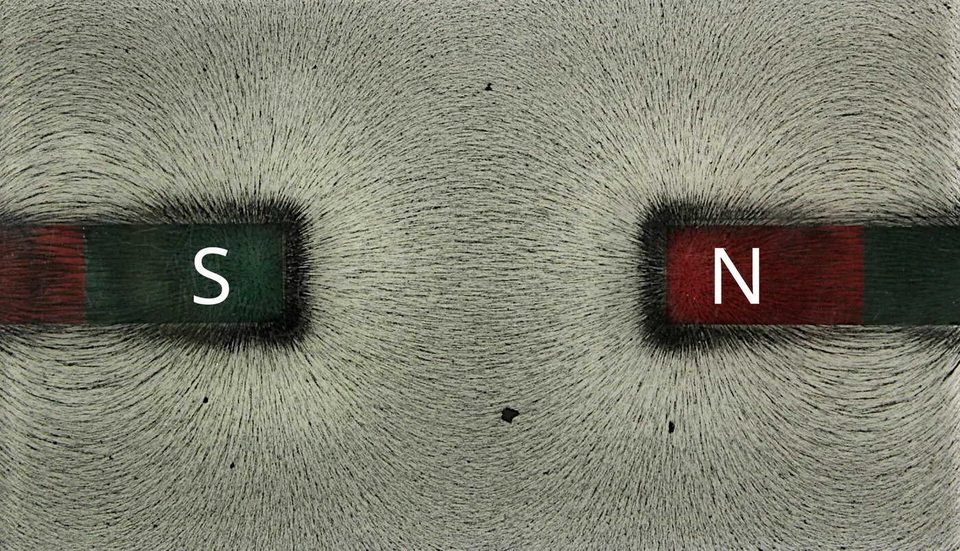 Two bar magnets with their south and north poles facing each other, surrounded by iron filings that form streaky patterns