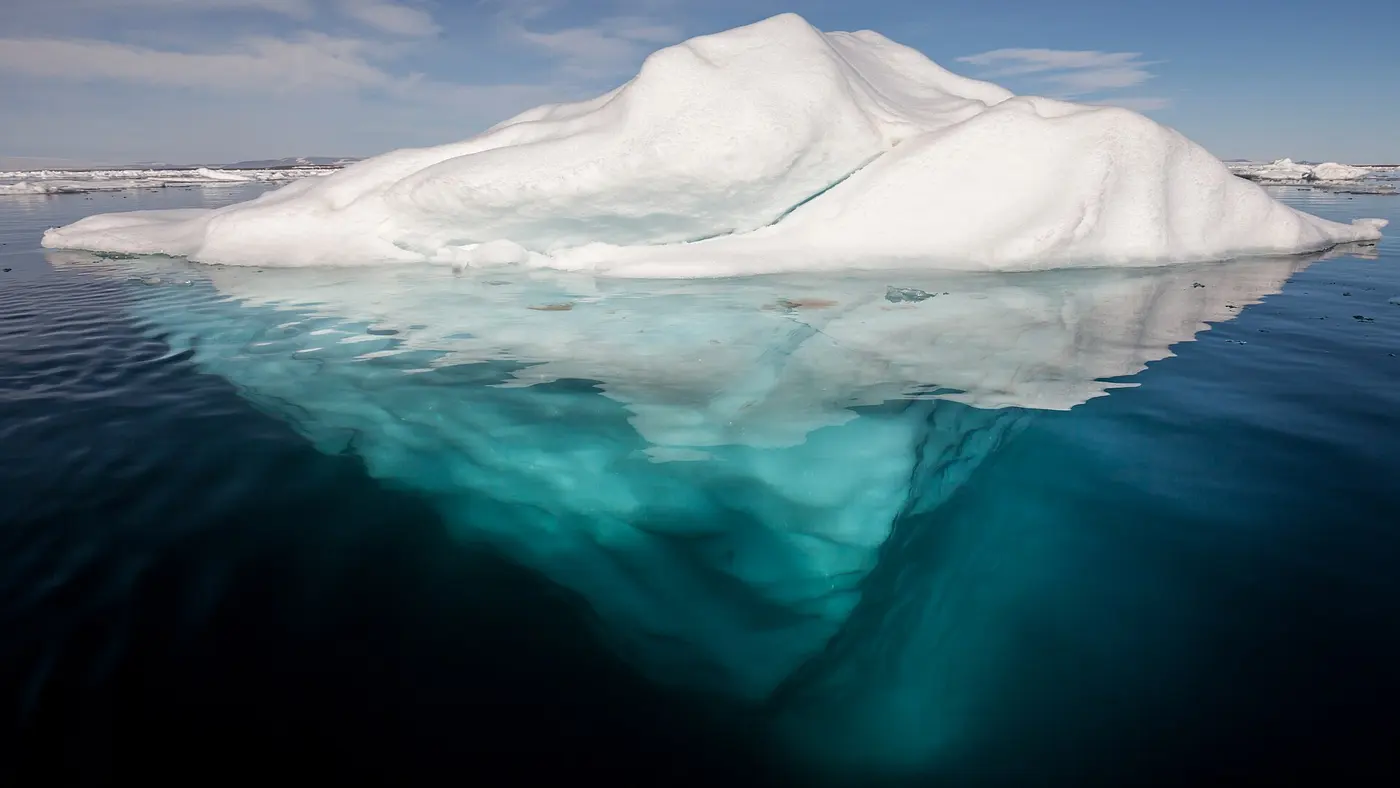 An iceberg floating in a calm Arctic sea, with a mass of ice much larger than the visible part showing through the water below