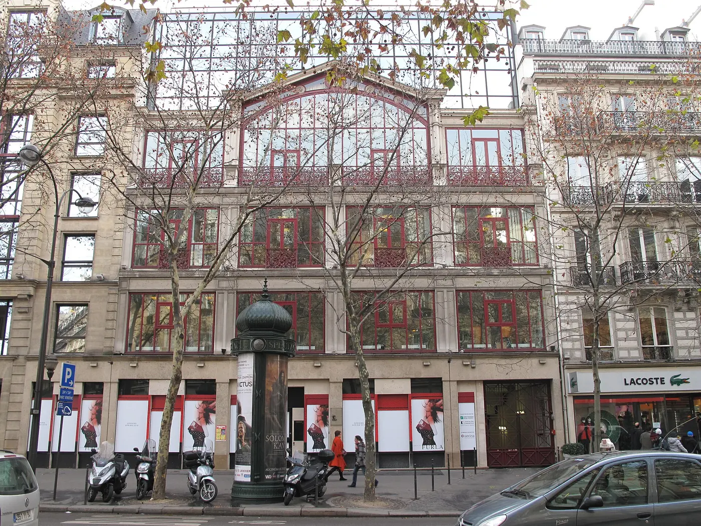 The front of a large glass-fronted building lined with red window frames
