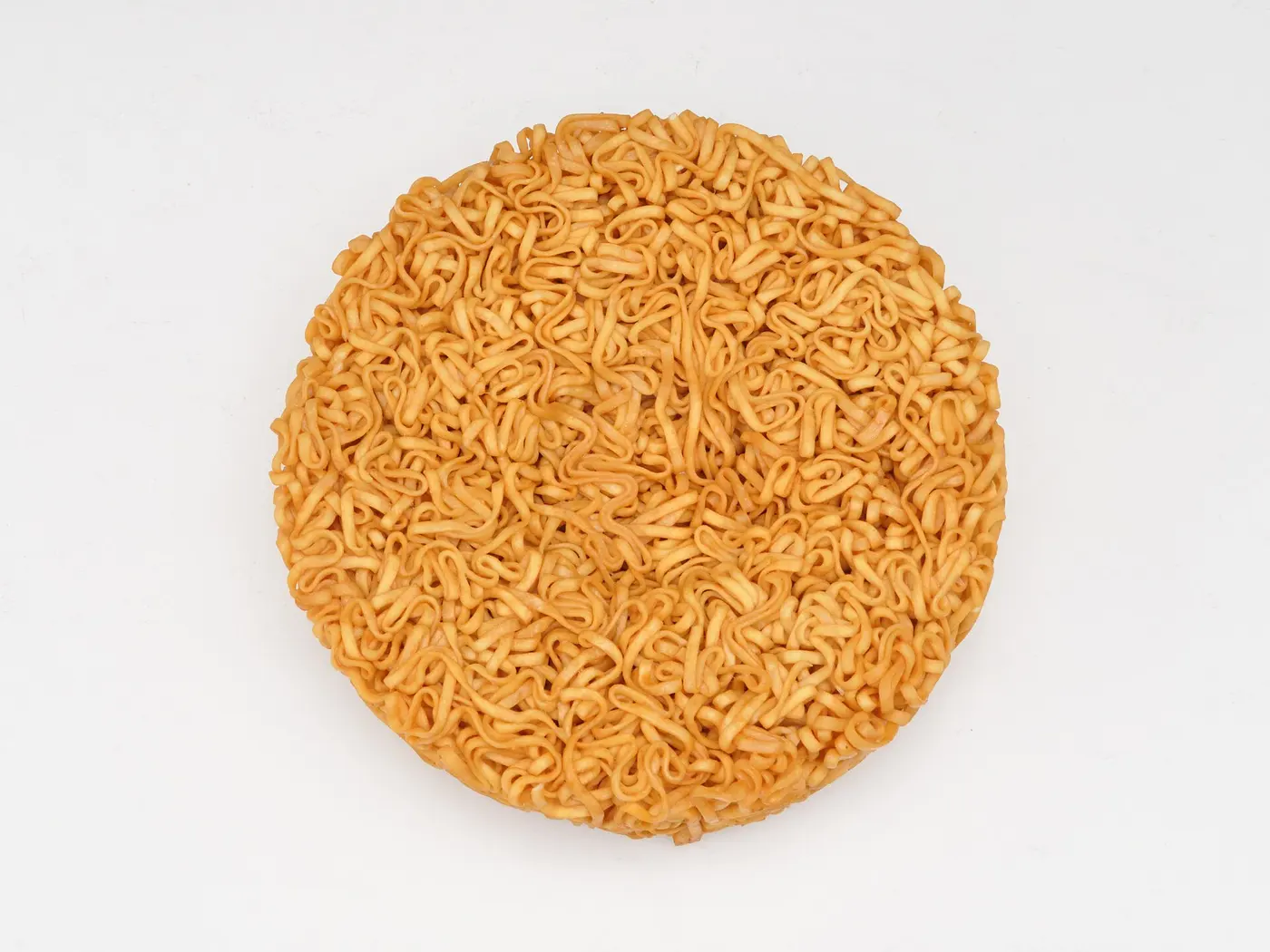 A golden, disc-shaped block of fried dried noodles on a white background