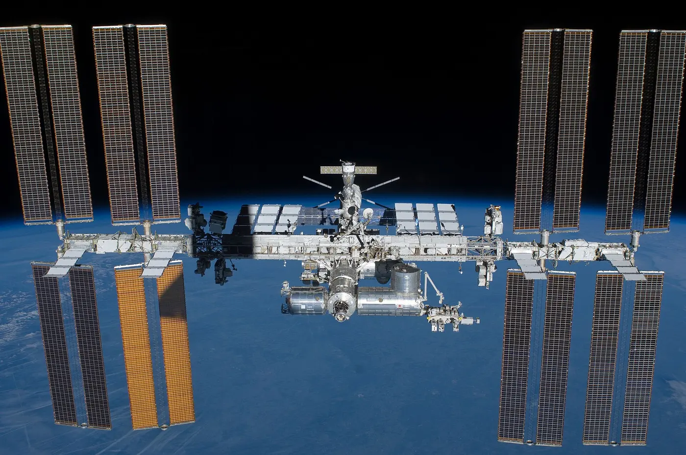 The International Space Station, its solar panels spread wide, flying against the blue Earth