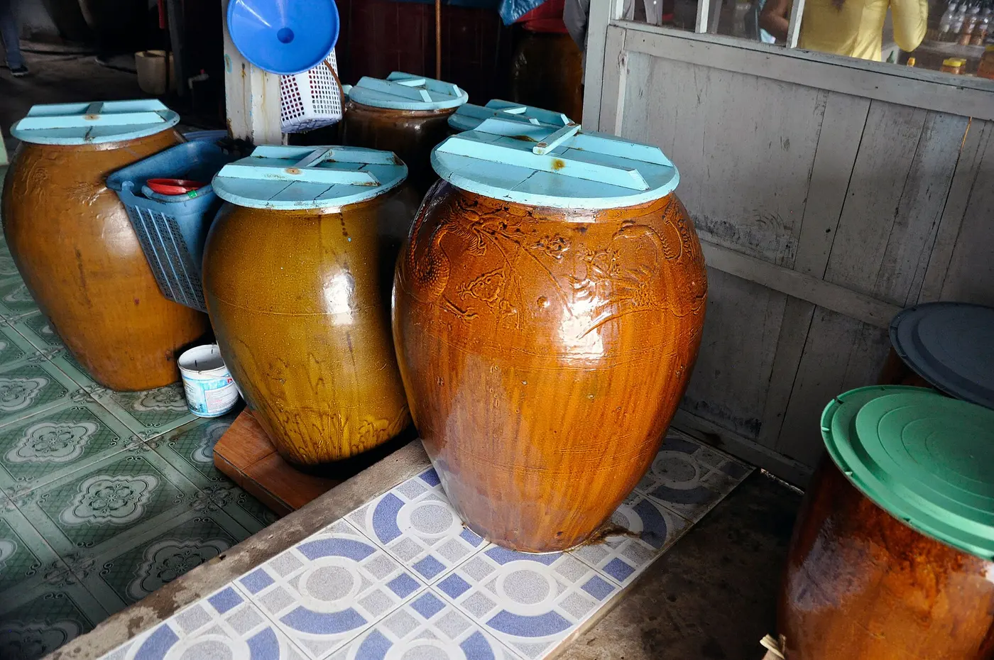 Large lidded brown earthenware jars standing on a tiled floor