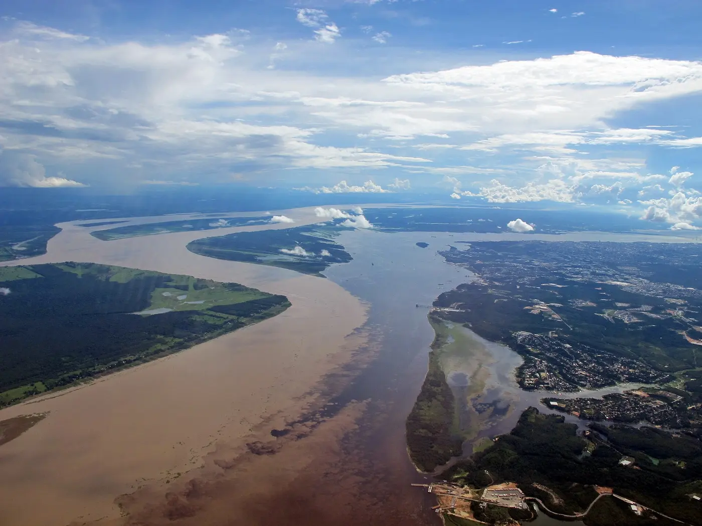 Aerial view of a muddy brown river and a dark river meeting and flowing side by side without immediately mixing
