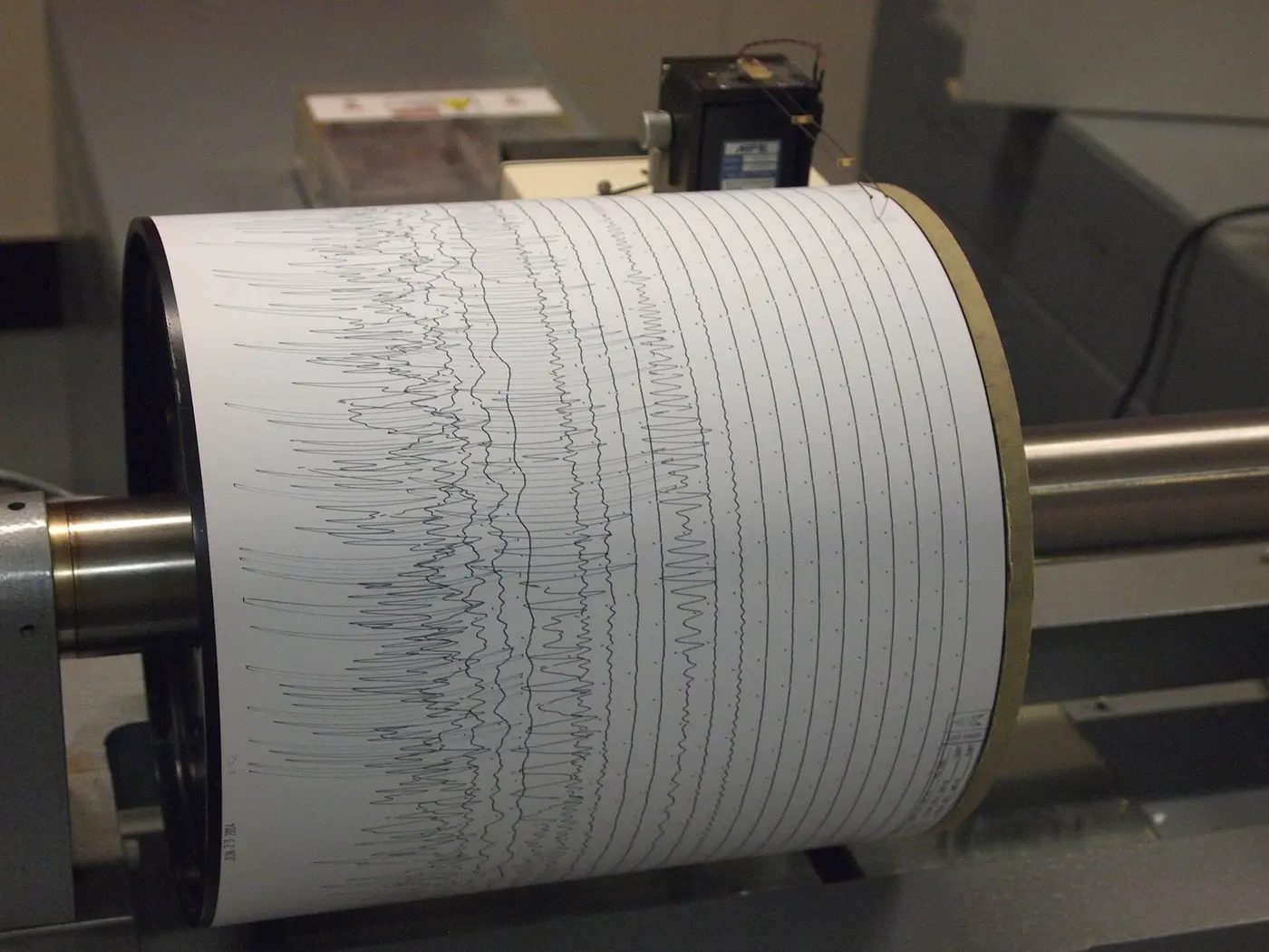 Recording paper wrapped around a rotating drum, covered with many finely wavering lines that trace earthquake shaking