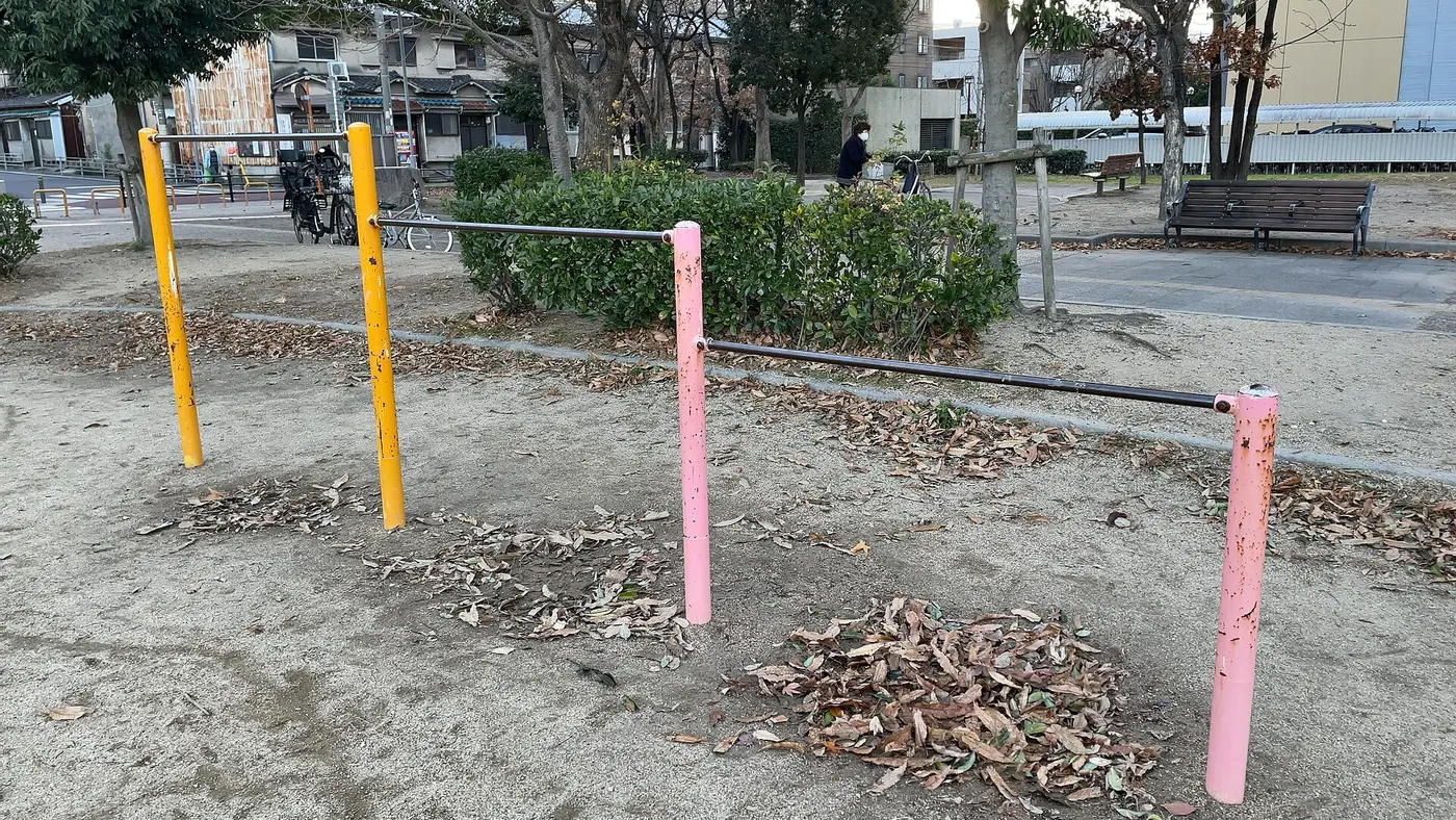 Horizontal bars of different heights in a park, with metal bars mounted on yellow and pink posts