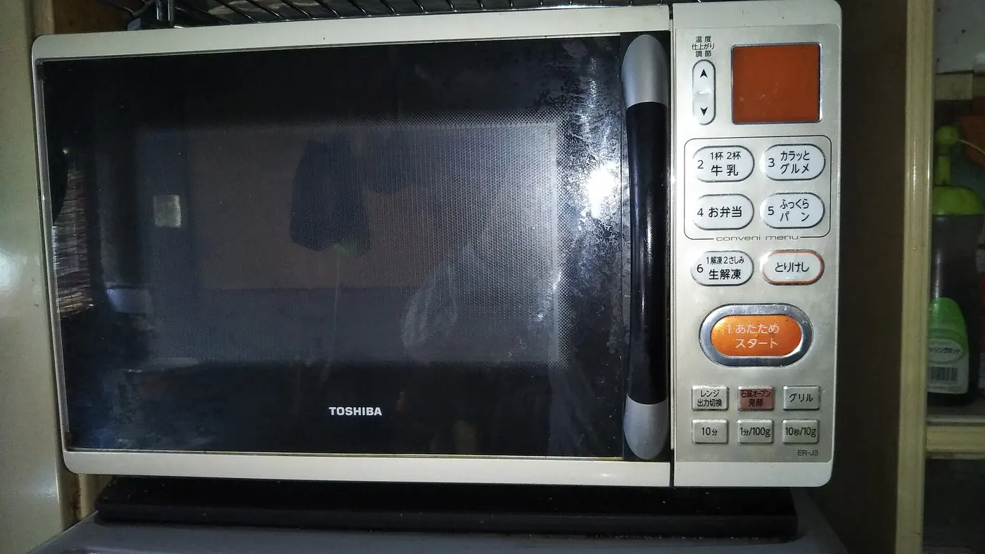 A household microwave oven seen from the front, with fine mesh visible in the window of its black door and buttons, including one for defrosting, lined up on the right