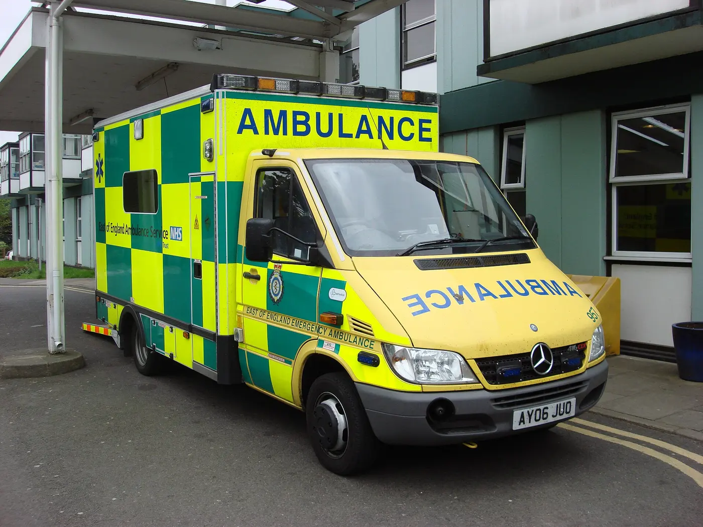 A yellow and green British ambulance with “AMBULANCE” written normally above the windshield and mirror-reversed on the hood