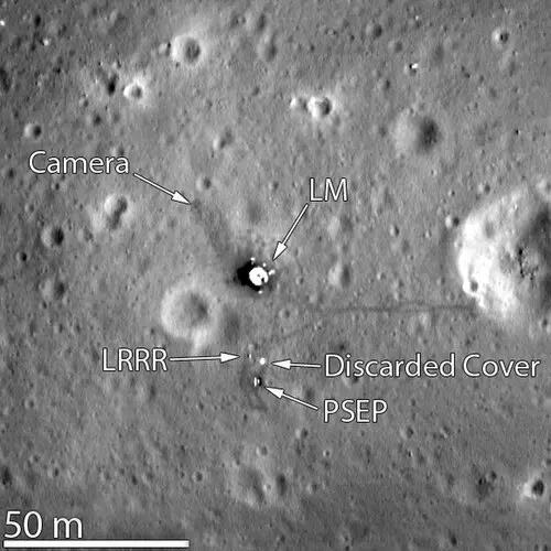 A gray lunar surface dotted with craters, with the bright dot of a lander in the center and a thin dark line running east from it toward a crater